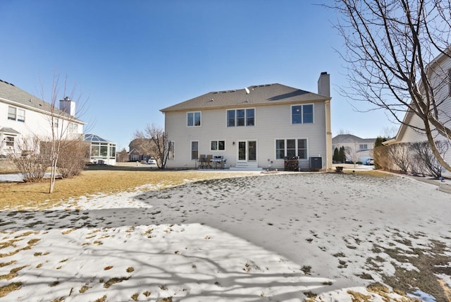 snow covered rear of property featuring central AC unit