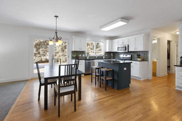 kitchen featuring white cabinetry, appliances with stainless steel finishes, decorative light fixtures, and a center island