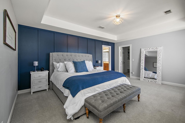 carpeted bedroom featuring a walk in closet, ensuite bathroom, a raised ceiling, and a closet