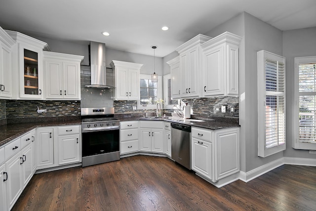 kitchen featuring pendant lighting, wall chimney range hood, appliances with stainless steel finishes, dark hardwood / wood-style floors, and white cabinets