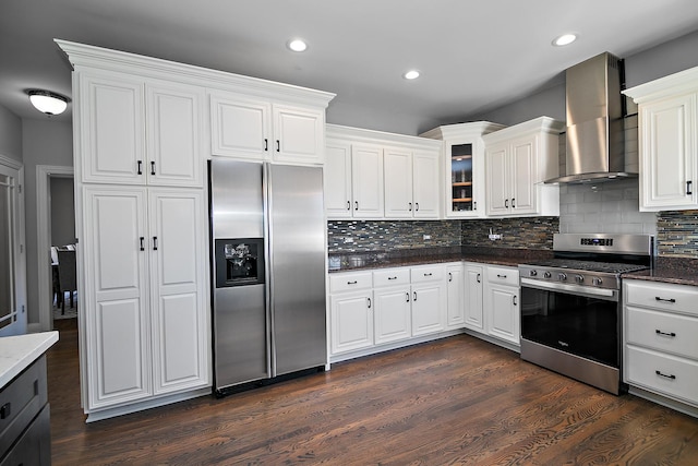 kitchen featuring appliances with stainless steel finishes, dark hardwood / wood-style floors, wall chimney range hood, decorative backsplash, and white cabinets