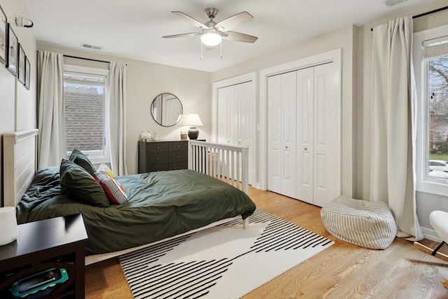 bedroom featuring ceiling fan, light hardwood / wood-style flooring, and multiple closets