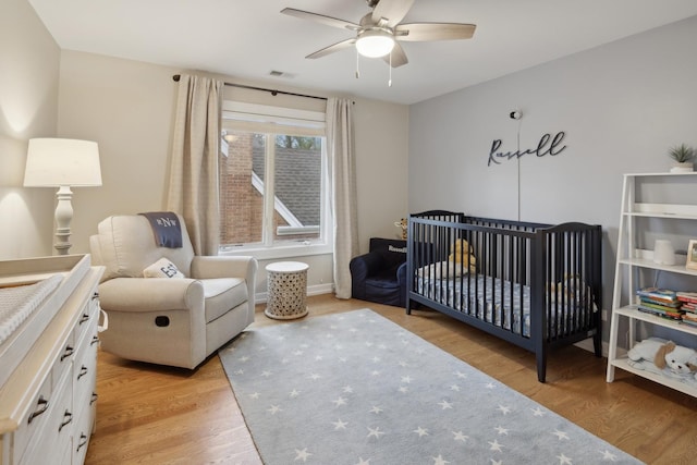 bedroom featuring a crib, light hardwood / wood-style flooring, and ceiling fan