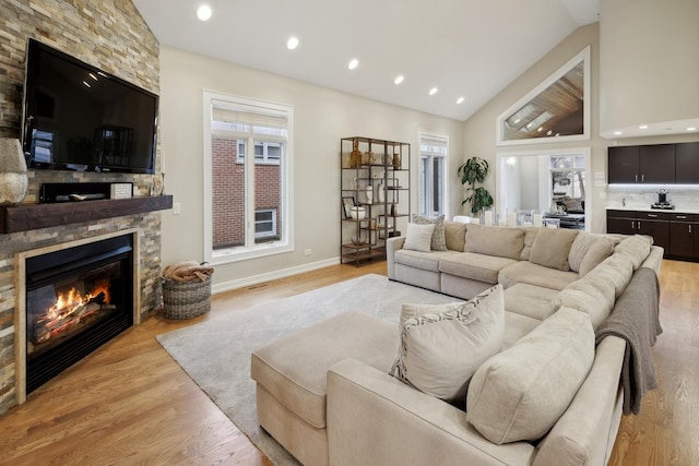 living room featuring a stone fireplace, high vaulted ceiling, and light wood-type flooring