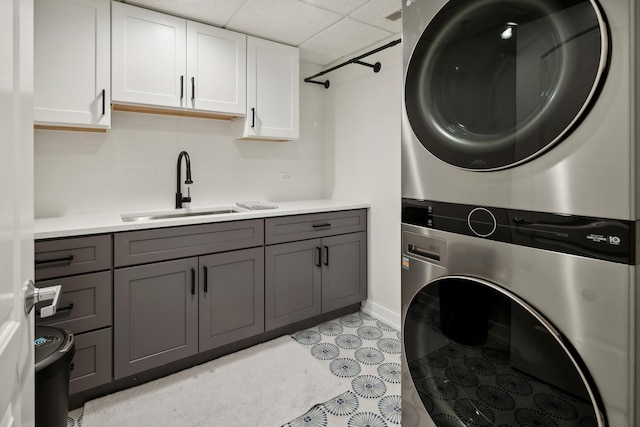 clothes washing area featuring sink, cabinets, and stacked washer and dryer