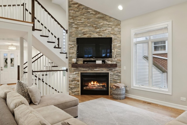 living room with high vaulted ceiling, a fireplace, and light hardwood / wood-style floors