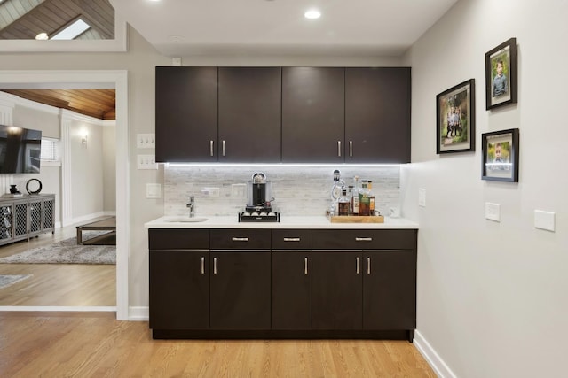 bar with dark brown cabinetry, sink, tasteful backsplash, and light wood-type flooring