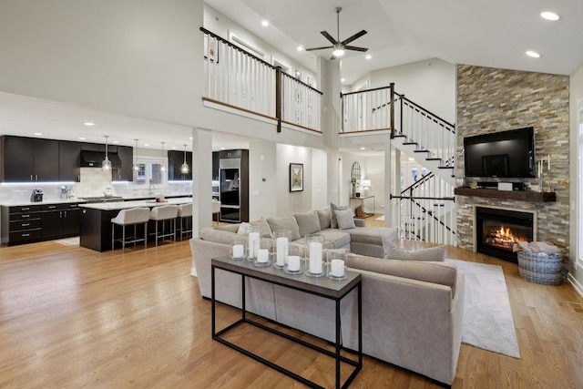 living room featuring high vaulted ceiling, a stone fireplace, light hardwood / wood-style floors, and ceiling fan