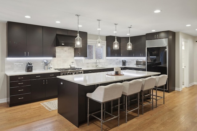 kitchen featuring a kitchen island, sink, hanging light fixtures, stainless steel appliances, and wall chimney range hood