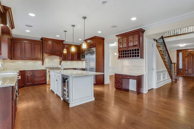 kitchen featuring crown molding, built in appliances, hanging light fixtures, dark hardwood / wood-style flooring, and a kitchen island with sink