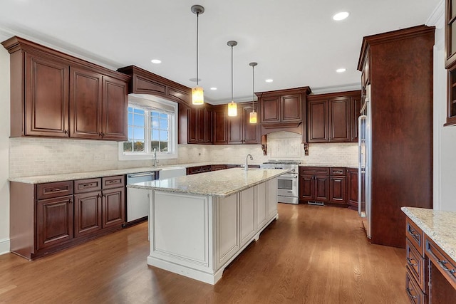 kitchen featuring dark wood-type flooring, hanging light fixtures, stainless steel appliances, light stone countertops, and a center island with sink