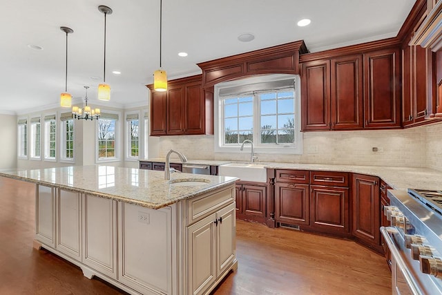 kitchen featuring decorative light fixtures, sink, high end stainless steel range oven, crown molding, and a center island with sink