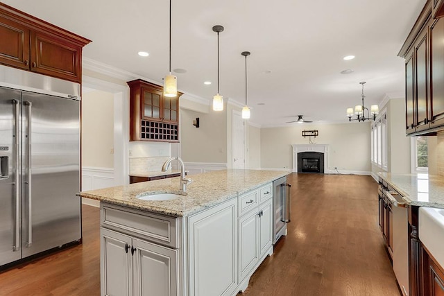 kitchen with sink, hanging light fixtures, ornamental molding, a center island with sink, and built in fridge