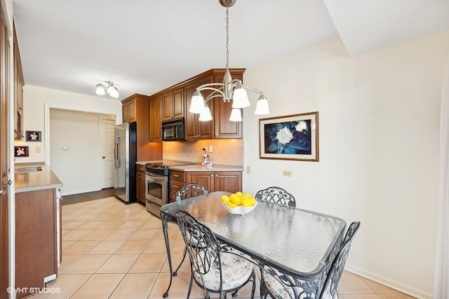 kitchen featuring appliances with stainless steel finishes, pendant lighting, backsplash, light tile patterned floors, and an inviting chandelier