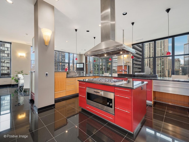 kitchen with hanging light fixtures, stainless steel appliances, island range hood, a kitchen island, and dark tile patterned flooring