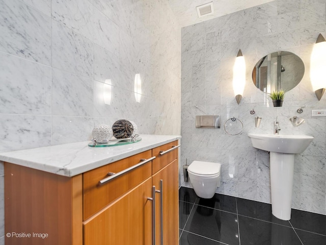 bathroom with tile patterned flooring, sink, toilet, and tile walls