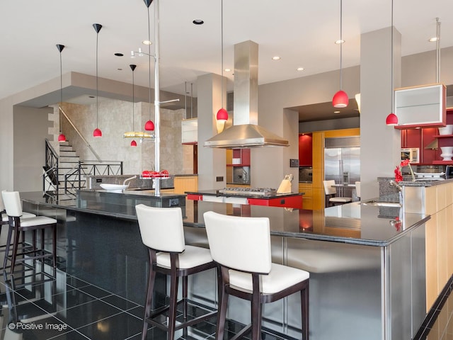 kitchen with a breakfast bar area, appliances with stainless steel finishes, hanging light fixtures, island range hood, and a kitchen island