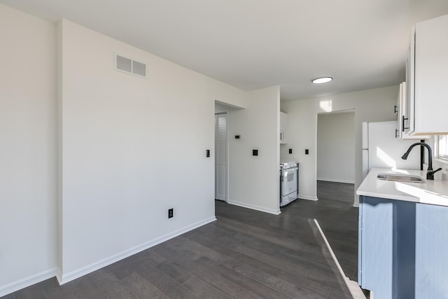 kitchen with white range with gas cooktop, sink, white cabinetry, and dark wood-type flooring