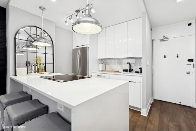 kitchen featuring sink, white cabinetry, stainless steel fridge, hanging light fixtures, and black electric cooktop