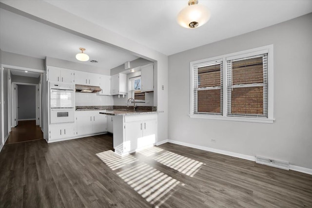 kitchen with white double oven, white cabinetry, dark stone countertops, dark hardwood / wood-style floors, and black cooktop