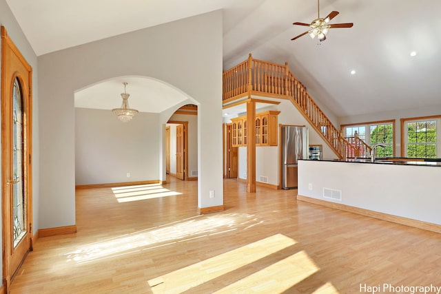 unfurnished living room with high vaulted ceiling, sink, ceiling fan with notable chandelier, and light wood-type flooring