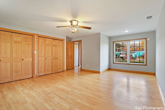 unfurnished bedroom featuring two closets, ceiling fan, and light wood-type flooring