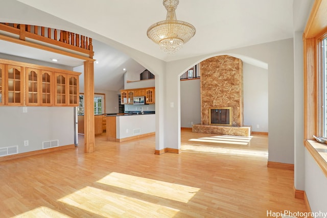 unfurnished living room featuring lofted ceiling, a large fireplace, sink, a chandelier, and light hardwood / wood-style flooring