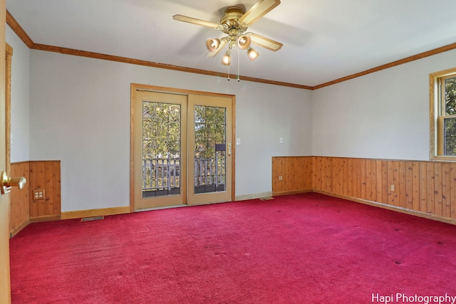 carpeted spare room with ornamental molding, ceiling fan, and wood walls