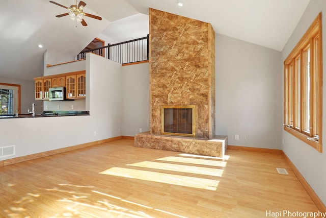 unfurnished living room featuring a premium fireplace, high vaulted ceiling, ceiling fan, and light hardwood / wood-style flooring