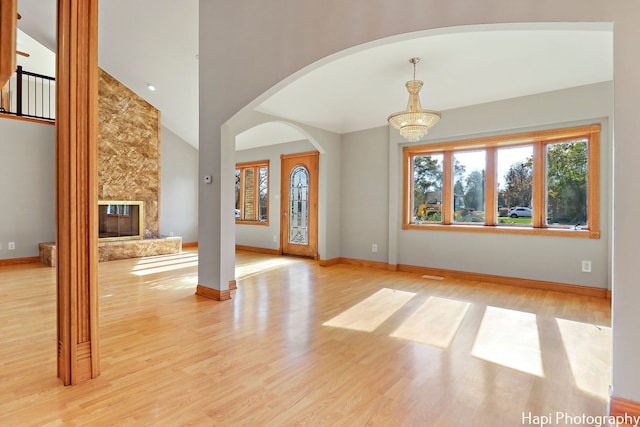 unfurnished living room with vaulted ceiling, a chandelier, a fireplace, and light hardwood / wood-style floors