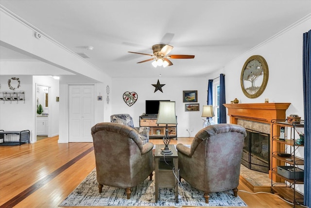 living room with a tiled fireplace, crown molding, light hardwood / wood-style flooring, and ceiling fan