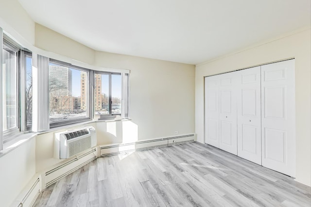 unfurnished bedroom featuring a baseboard heating unit, a wall mounted AC, a closet, and light wood-type flooring