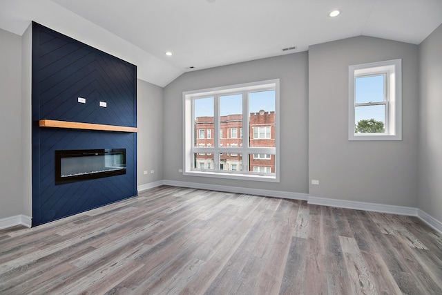 unfurnished living room featuring a large fireplace, lofted ceiling, and light hardwood / wood-style flooring