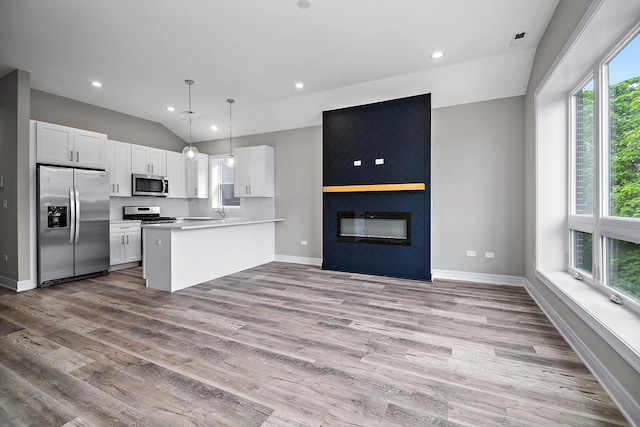 kitchen featuring appliances with stainless steel finishes, pendant lighting, white cabinetry, lofted ceiling, and kitchen peninsula