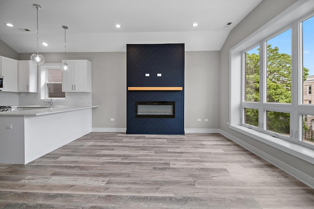 kitchen with lofted ceiling, sink, white cabinetry, light wood-type flooring, and pendant lighting