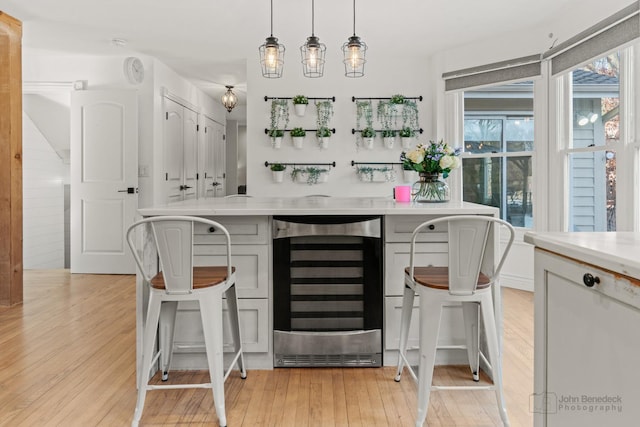 bar featuring white cabinetry, beverage cooler, light hardwood / wood-style floors, and decorative light fixtures