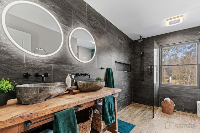 bathroom with hardwood / wood-style floors, a tile shower, tile walls, decorative backsplash, and vanity