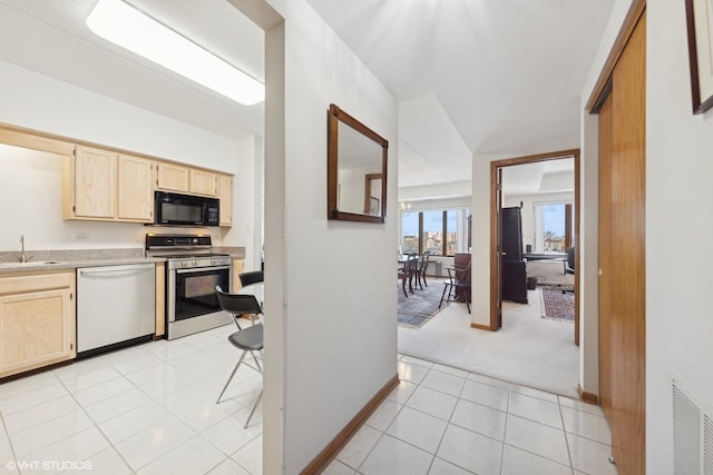 kitchen featuring stainless steel gas range, light tile patterned flooring, dishwasher, and light brown cabinets