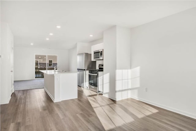 kitchen featuring sink, white cabinets, a kitchen island with sink, stainless steel appliances, and light wood-type flooring