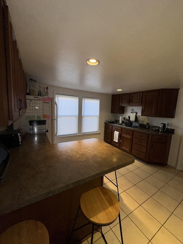 kitchen featuring light tile patterned flooring, a kitchen bar, kitchen peninsula, and white fridge