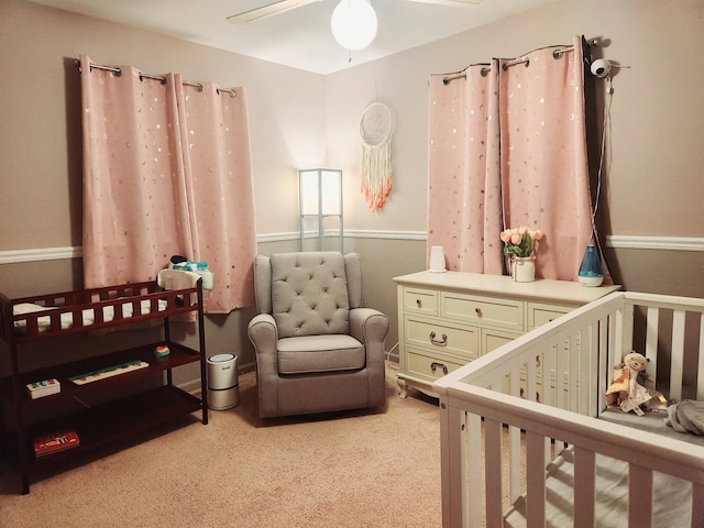 bedroom featuring light carpet, a nursery area, and ceiling fan