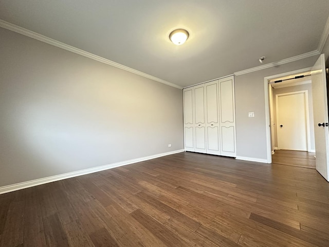 unfurnished bedroom featuring ornamental molding, a barn door, dark hardwood / wood-style floors, and a closet