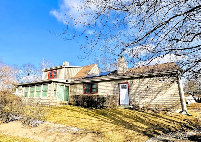 back of property featuring a yard and solar panels