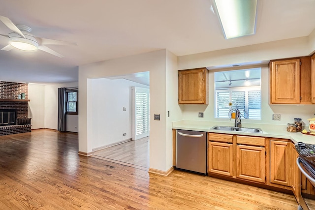 kitchen with sink, light hardwood / wood-style flooring, ceiling fan, appliances with stainless steel finishes, and a fireplace