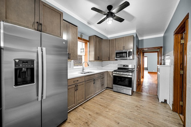 kitchen with appliances with stainless steel finishes, sink, backsplash, ceiling fan, and light hardwood / wood-style flooring