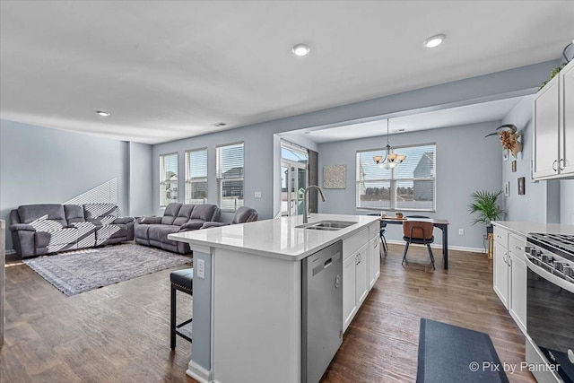 kitchen with appliances with stainless steel finishes, white cabinetry, sink, hanging light fixtures, and a kitchen island with sink