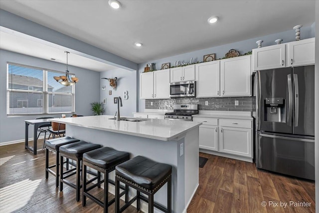 kitchen featuring appliances with stainless steel finishes, decorative light fixtures, an island with sink, sink, and white cabinets