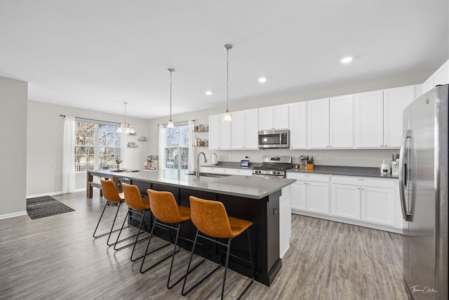 kitchen featuring light wood finished floors, stainless steel appliances, white cabinetry, a sink, and a kitchen bar