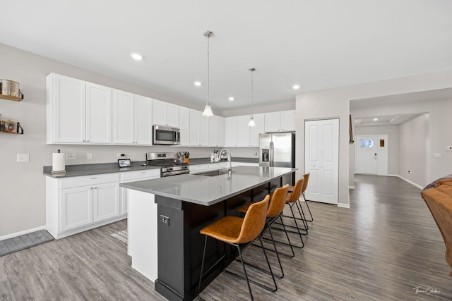 kitchen featuring white cabinets, a breakfast bar, wood finished floors, stainless steel appliances, and a sink