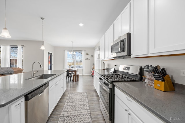 kitchen featuring wood finished floors, a sink, white cabinetry, appliances with stainless steel finishes, and dark stone countertops